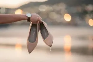 Scarpe beige bagnate tenute in mano al tramonto.