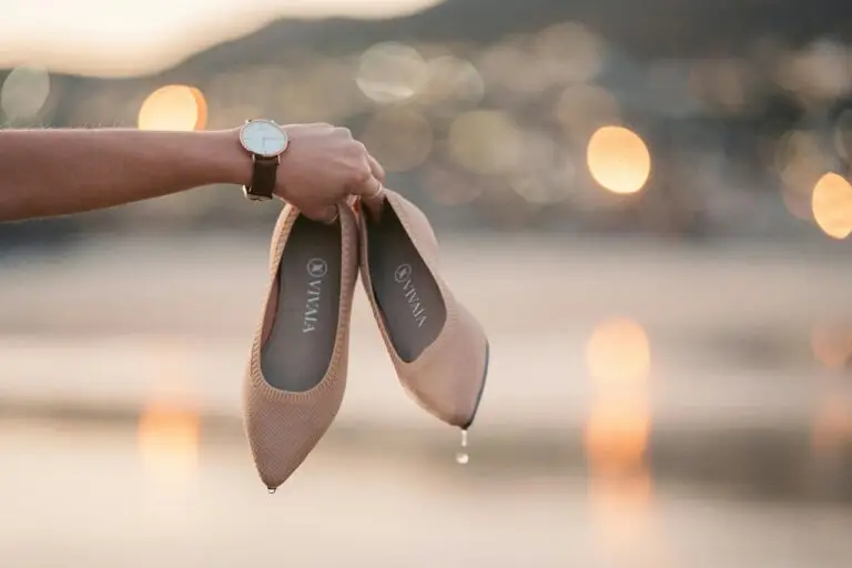 Scarpe beige bagnate tenute in mano al tramonto.